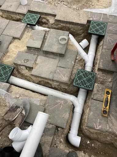 PVC drainage pipes and green catch basins set in a paver patio