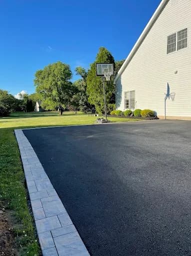 Fresh asphalt driveway and basketball area with stone paver border