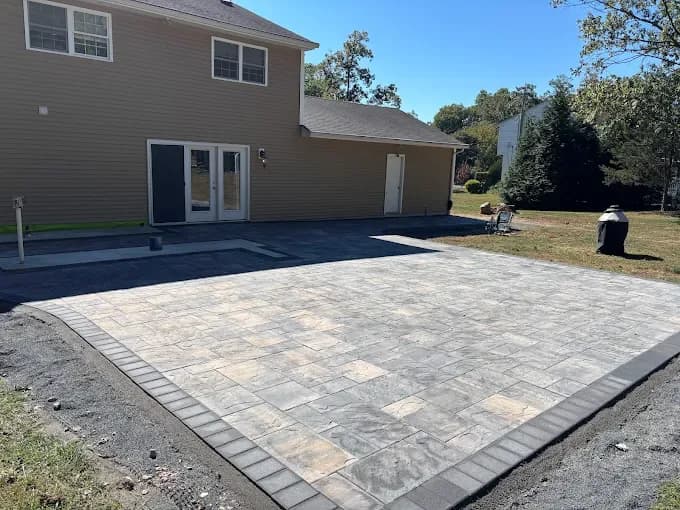 Large multi-toned paver patio with charcoal border behind a home