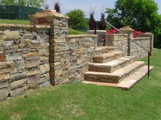 Natural stone retaining wall with integrated stairs and metal handrail